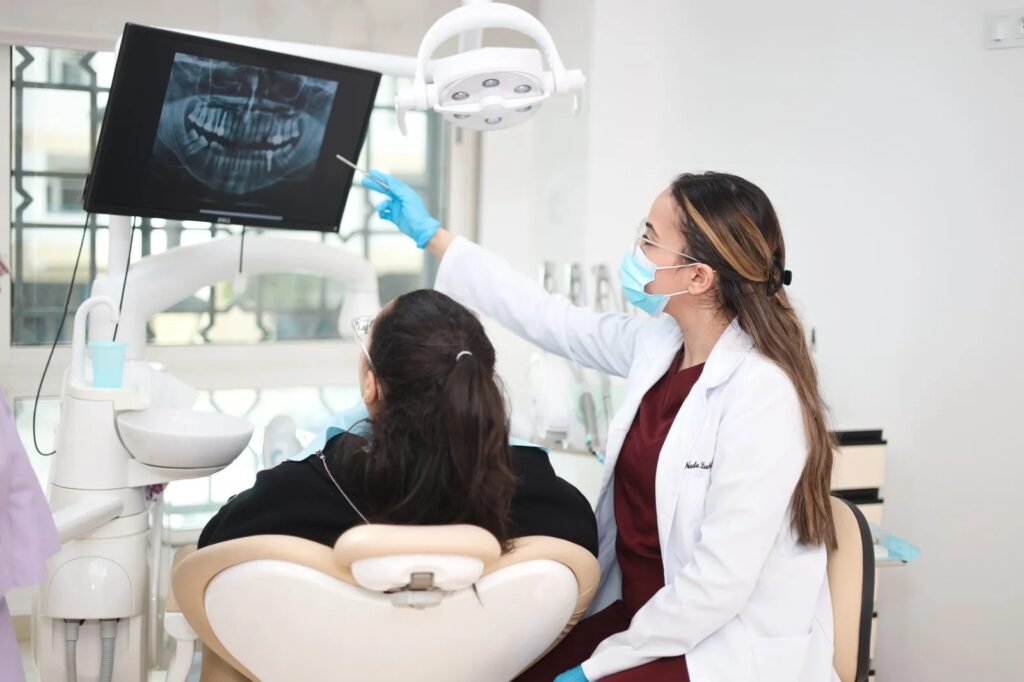 Dentiste montrant une radiographie dentaire sur écran à une patiente assise au fauteuil lors d’une consultation