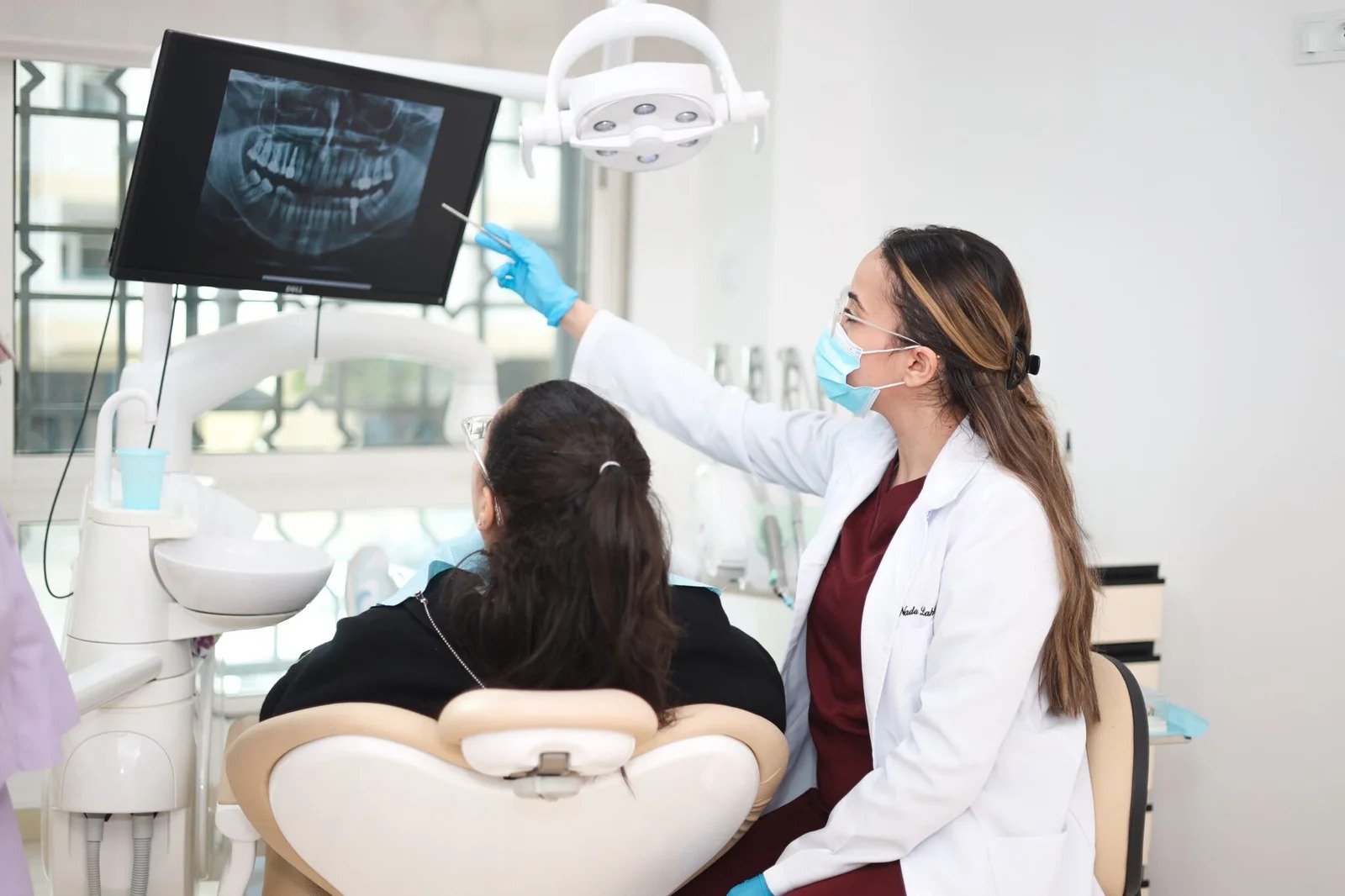 Dentiste montrant une radiographie dentaire sur écran à une patiente assise au fauteuil lors d’une consultation