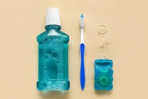 Bain de bouche, brosse à dents et fil dentaire disposés sur un fond beige pour illustrer une routine d’hygiène bucco-dentaire quotidienne.