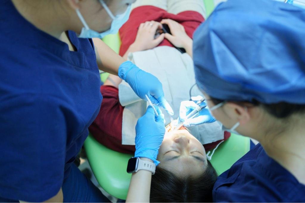 Équipe dentaire réalisant un traitement de carie dentaire sur une patiente dans un cabinet équipé de matériel de soins modernes.