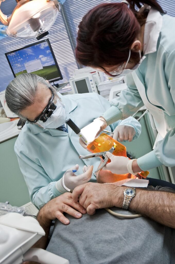 Dentistes réalisant un traitement dentaire avec lampe de polymérisation dans un cabinet équipé pour les soins et prothèses dentaires esthétiques.