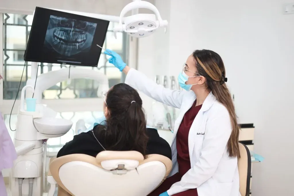 Dentiste expliquant un traitement d’esthétique dentaire et Hollywood Smile à une patiente dans une clinique dentaire moderne équipée d’un écran radiographique.