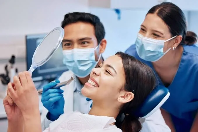Patiente souriante admirant le résultat de son nettoyage dentaire dans le miroir avec son médecin dentiste